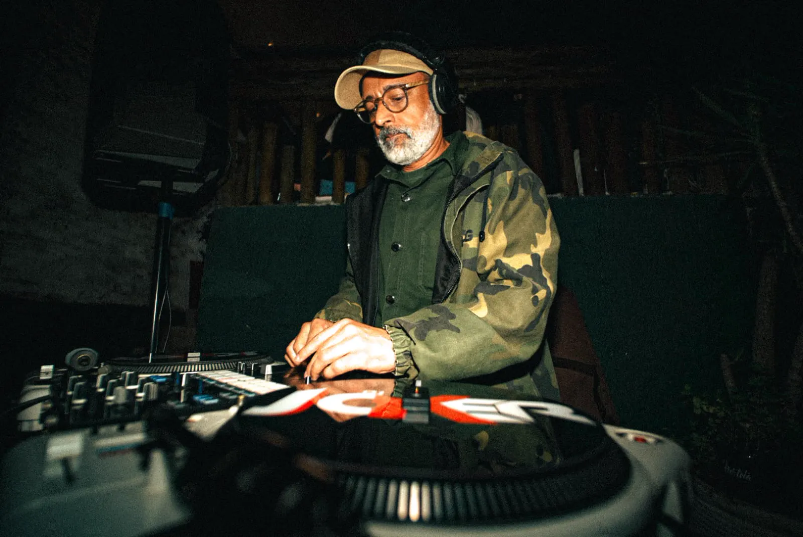 DJ tocando na cabine montada na casa, de fone e boné, com as mãos sobre o controlador.